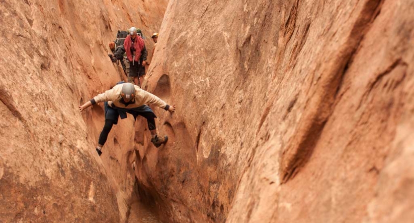A person braces themselves on opposite walls of a slot canyon